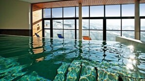 An indoor swimming pool with clear water, large windows, and a view of snow-covered mountains.