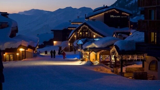 A snow-covered village with wooden buildings and a mountain backdrop.