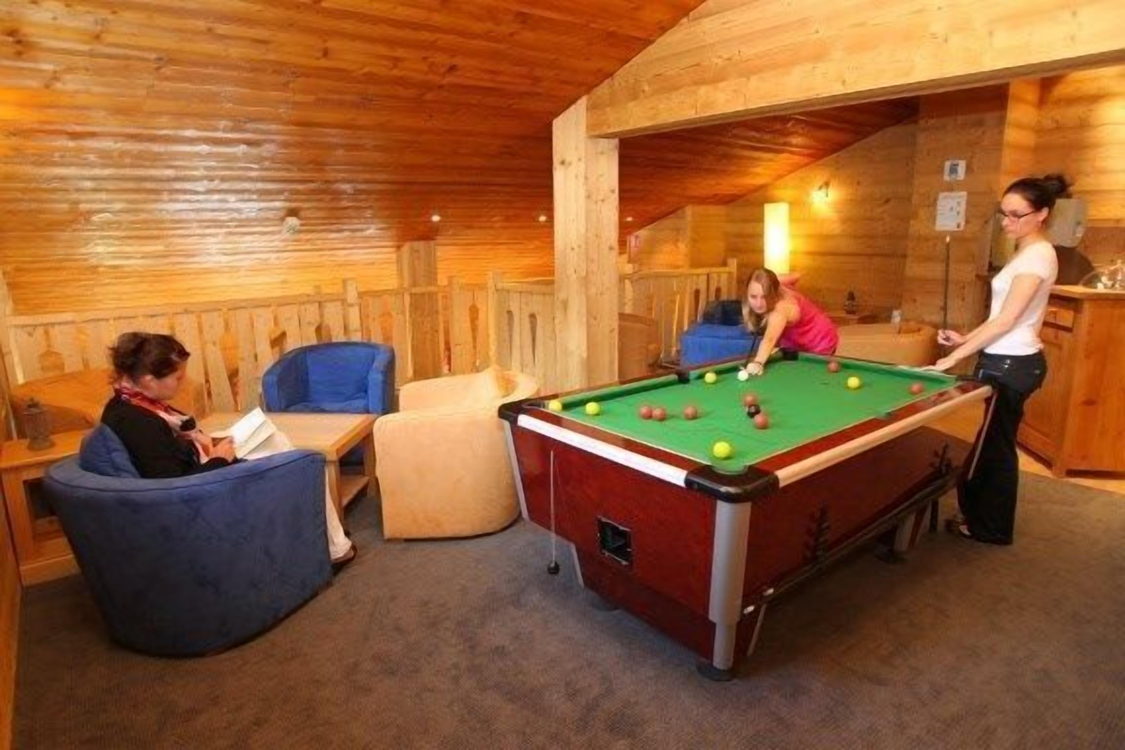 Ein Holzinnenraum mit Billardtisch, Sitzgelegenheiten und einer Bar.