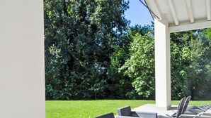 Una veranda esterna con mobili in vimini, una zona coperta e un prato curato.