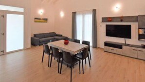 Un soggiorno moderno con zona pranzo, un divano grigio, una TV a schermo piatto e un camino.