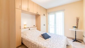 Une chambre à coucher avec un lit, des armoires en bois, une petite table avec un vase et une fenêtre avec des stores.