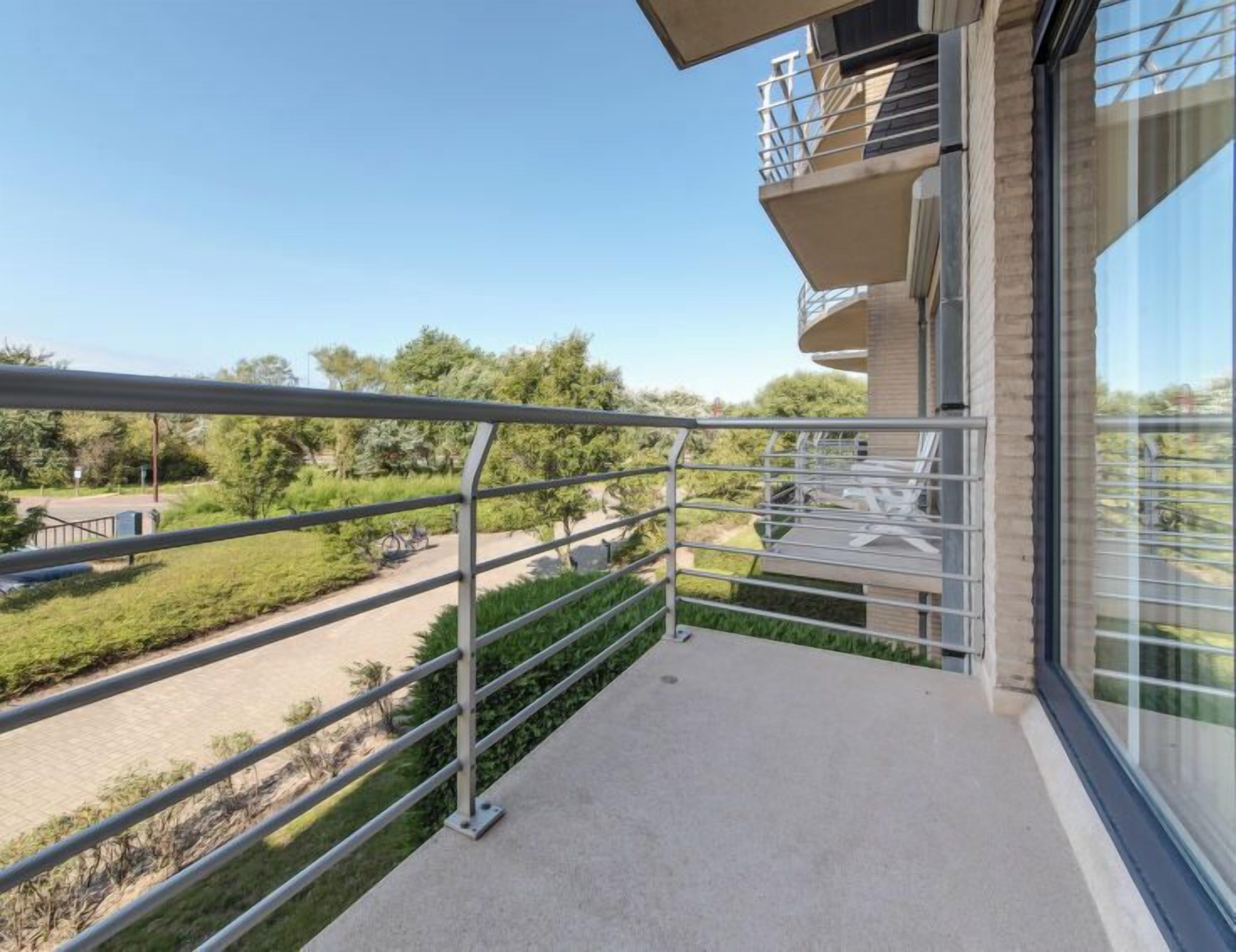 A balcony with a metal railing overlooking a road and greenery.