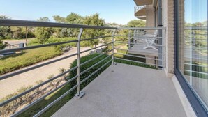 Un balcon doté d’une rambarde en métal, donnant sur une route et sur de la verdure.