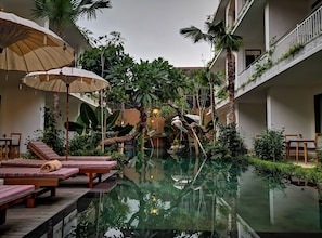 An indoor pool with lounge chairs and umbrellas, surrounded by lush greenery and plants. - Sabana Ubud (Ubud)