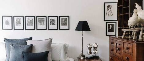 A bedroom with a bed, pillows, a nightstand with a lamp, a dresser, and framed pictures on the wall.