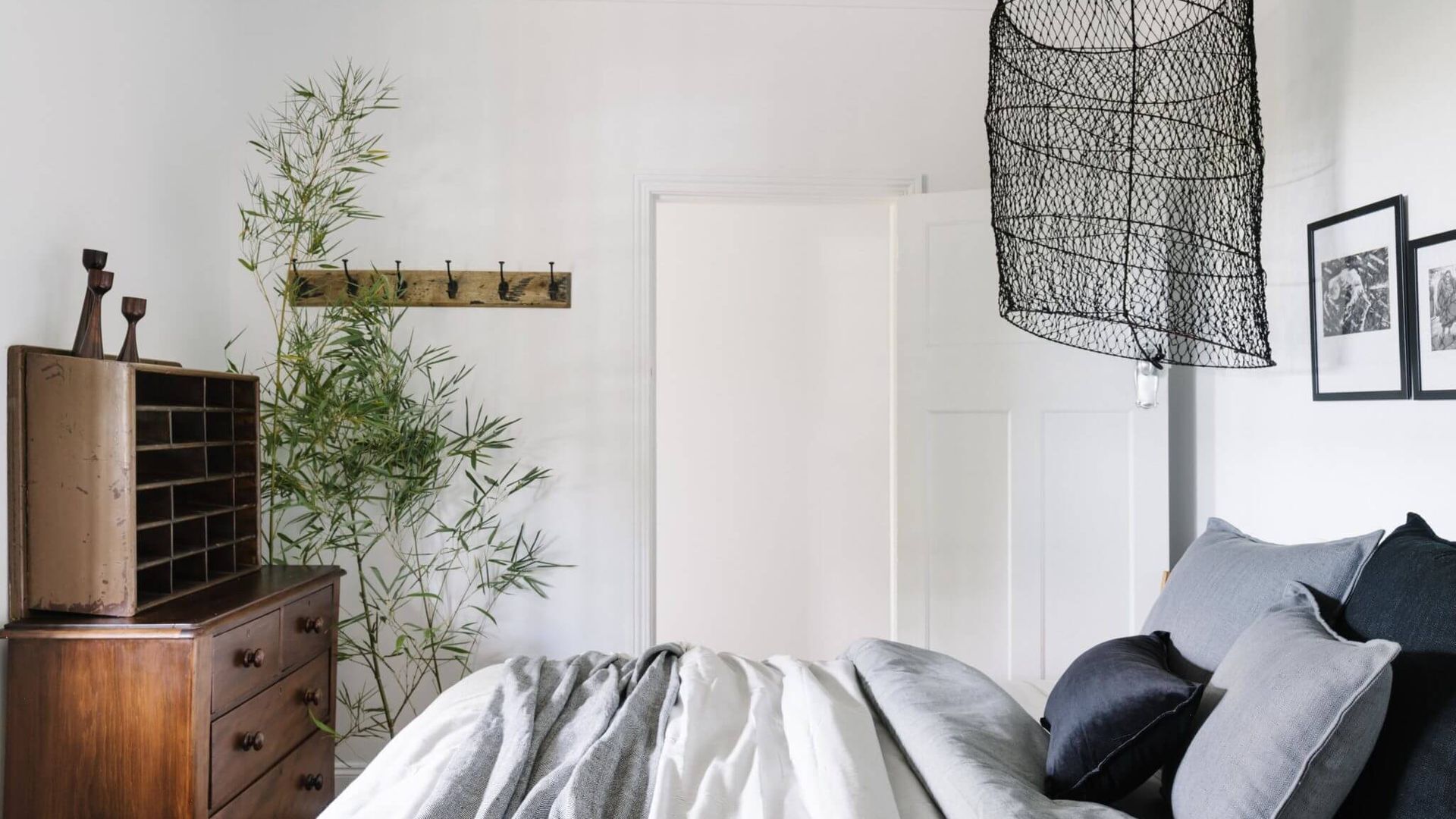 Ein Schlafzimmer mit Bett, Schminktisch, einer Bambuspflanze, einer Hängelampe und einer Tür.