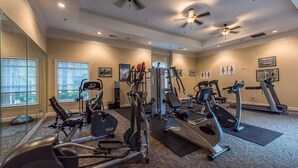 A well-equipped gym with various exercise machines, large windows, and ceiling fans. - Magical Tuscan Experience (Champions Gate)