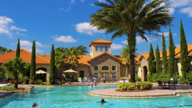 A resort with a swimming pool, palm trees, and a building with a red-tiled roof. - Magical Tuscan Experience (Champions Gate)
