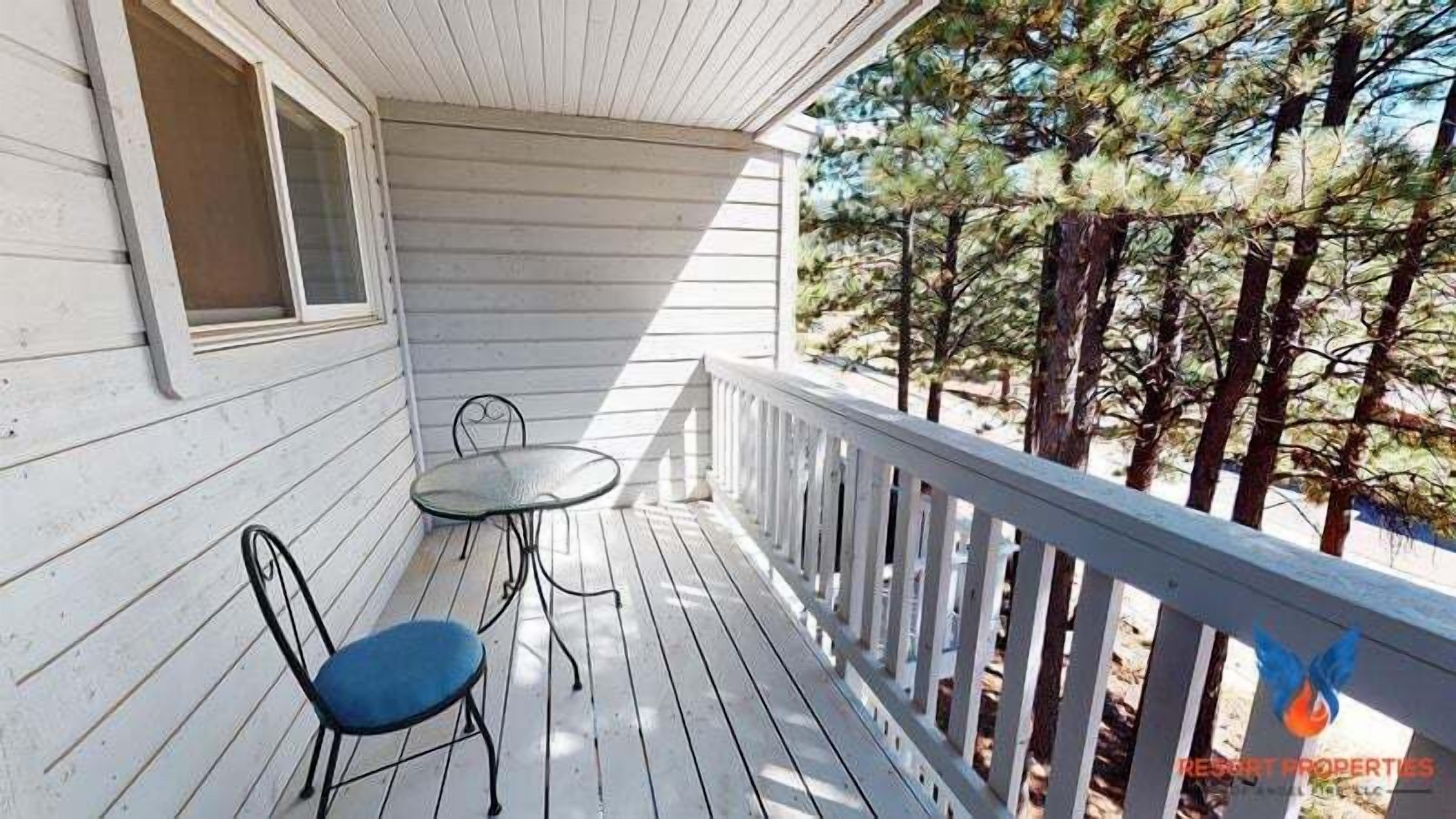 A wooden deck with a railing, a table, and two chairs.