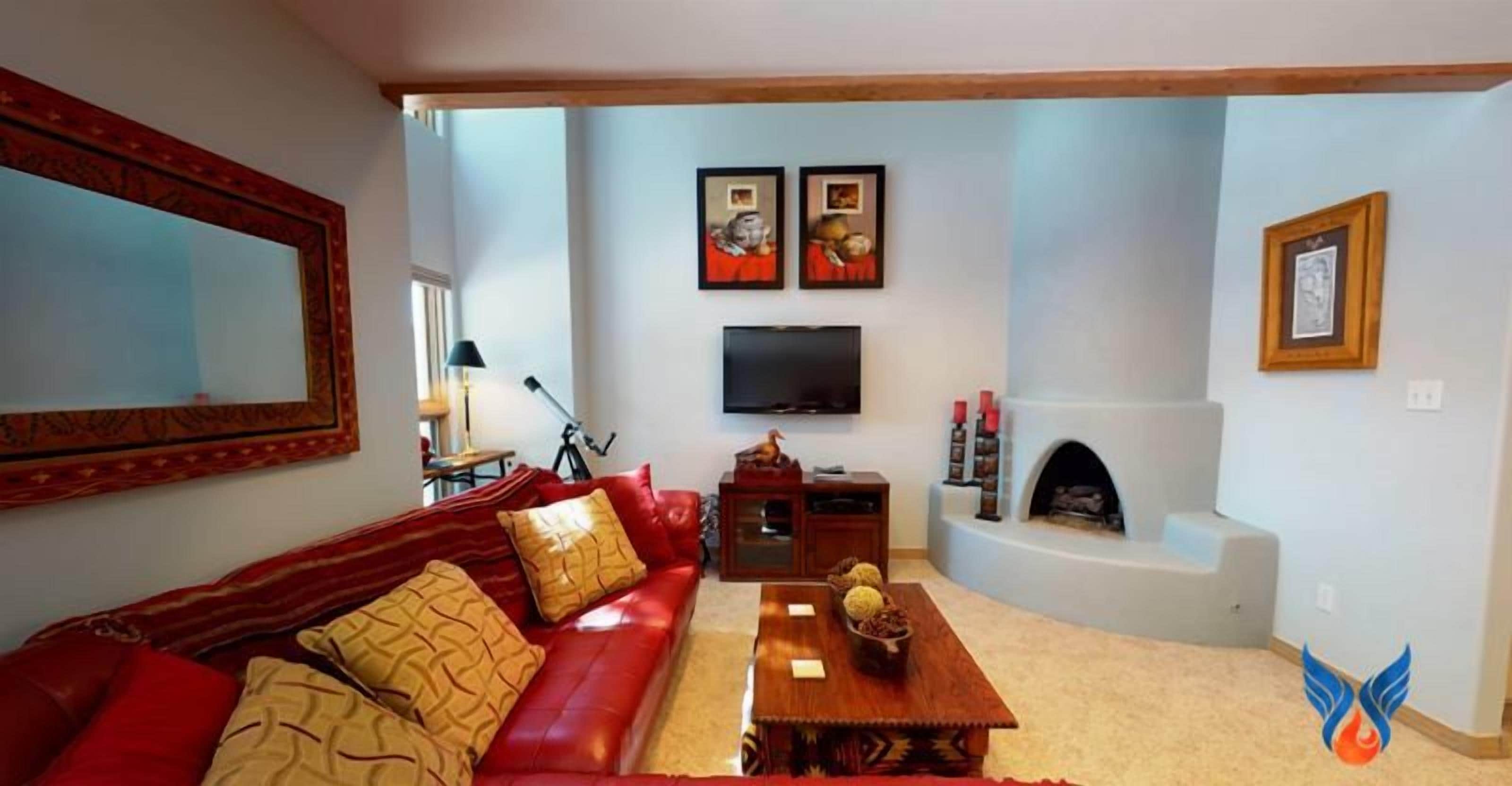 Un salon avec un canapé en cuir rouge, une table basse en bois, une cheminée et un téléviseur fixé au mur.