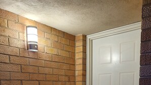 A corner of a room with a white door, a textured brick wall, and a wall-mounted light fixture.