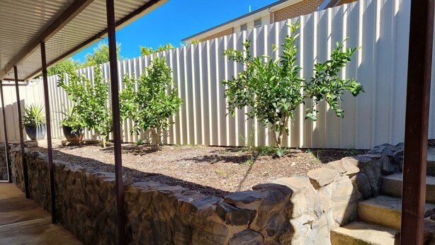 A covered outdoor area with stone walls, potted plants, and steps leading to a building.