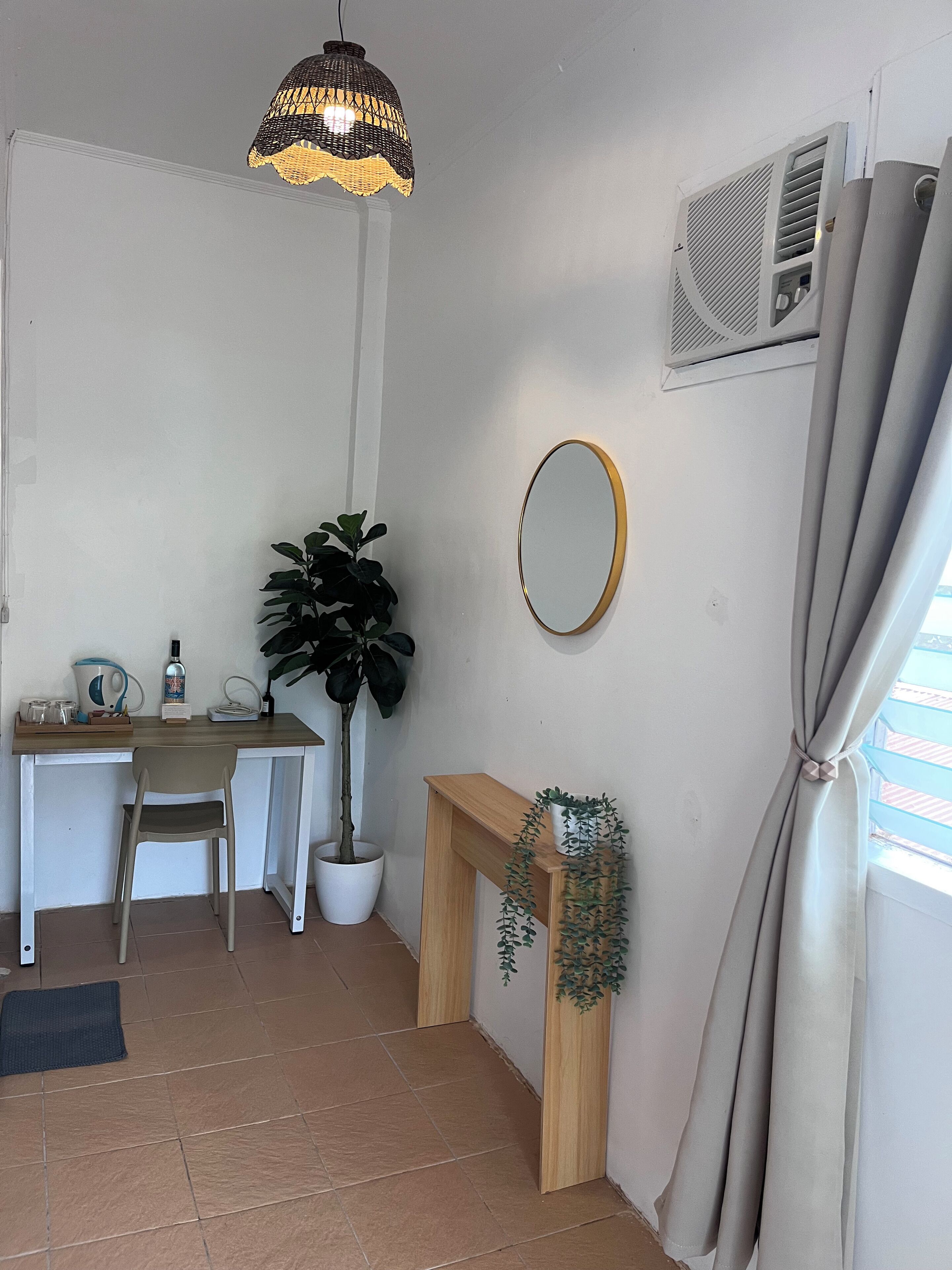 A small room with a desk, chair, potted plant, mirror, and a hanging light fixture.