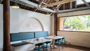 A restaurant interior with a wooden ceiling, a neon sign reading "The Shark's Tale", a blue bench, and a table with chairs.