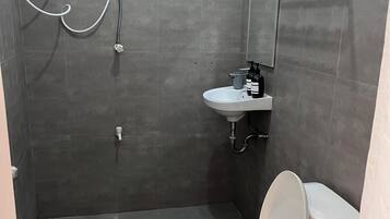 A compact bathroom with a white toilet, a small sink, and a shower area.