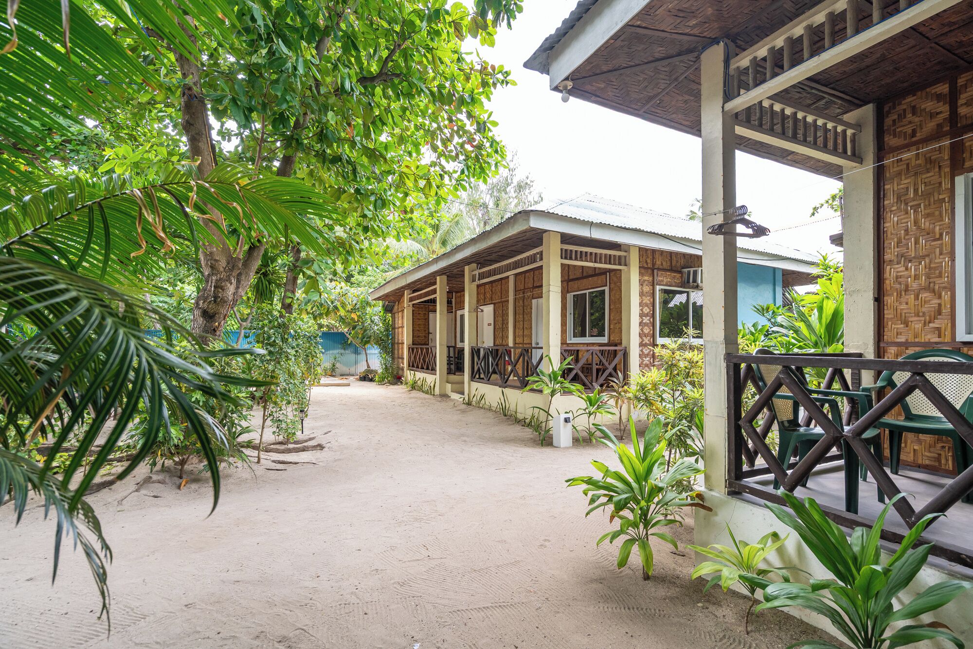 A building with a covered porch and a sandy courtyard surrounded by greenery.