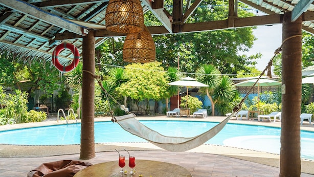 A poolside area with a hammock, lounge chairs, and a table with drinks.