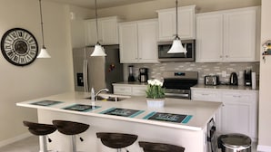 A modern kitchen with white cabinets, stainless steel appliances, a central island with bar stools, and a decorative clock. - Solterra Resort - is a beautiful paradise located in Davenport, near to Orlando (Davenport)