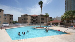A swimming pool surrounded by apartment buildings, with a palm tree in the center. - Waipani E14-2BR -Beach Across The Street-Pool (North Myrtle Beach)