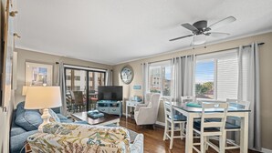 A living room with a sofa, a coffee table, a TV, and a dining area with a table and chairs. - Waipani E14-2BR -Beach Across The Street-Pool (North Myrtle Beach)