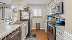 A modern kitchen with granite countertops, stainless steel appliances, and a small trash can. - Waipani E14-2BR -Beach Across The Street-Pool (North Myrtle Beach)