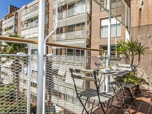 A balcony with a metal railing, a table with chairs, and potted plants.