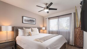 Une chambre bien rangée, avec un lit, des lampes de chevet, un ventilateur de plafond et une fenêtre avec des rideaux.