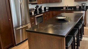 Une cuisine moderne avec des meubles en bois, des appareils en acier inoxydable et un îlot central doté de tabourets de bar.