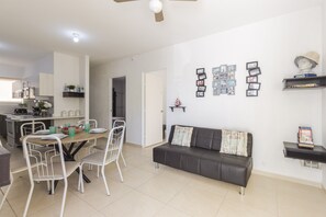 A modern living room with a dining area, a black leather sofa, and a ceiling fan.