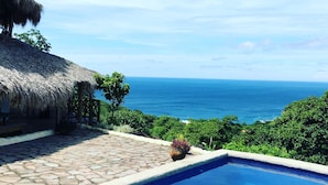 Ein Pool mit Blick auf das Meer, eine mit Reet gedeckte Struktur und üppiges Grün.