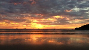 Ein Strand bei Sonnenuntergang, ruhiges Wasser spiegelt den Himmel wider.