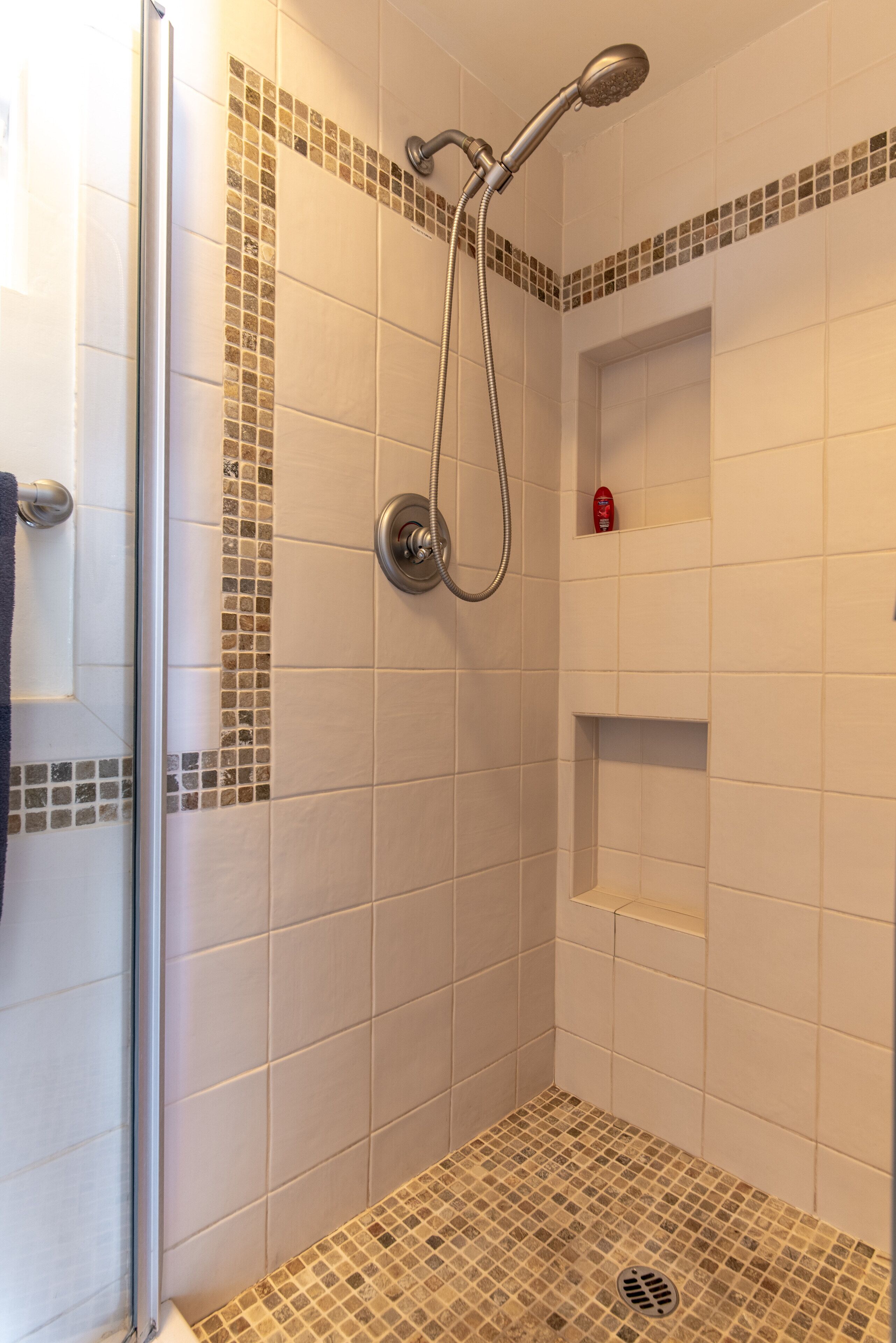 A shower with a handheld showerhead, a glass door, and a tiled floor with a mosaic pattern.