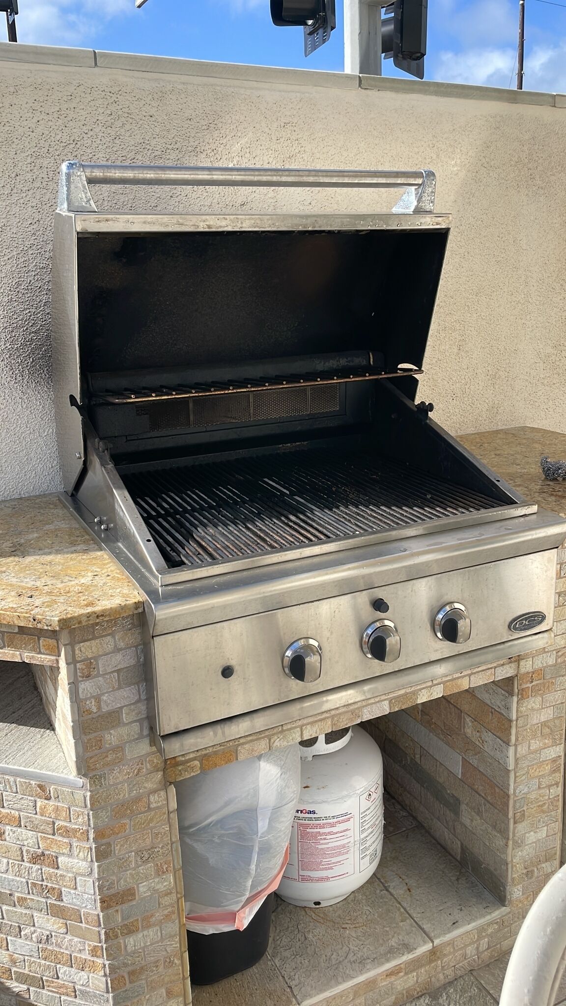 Una parrilla exterior sobre base de ladrillo y un tanque de gas debajo.