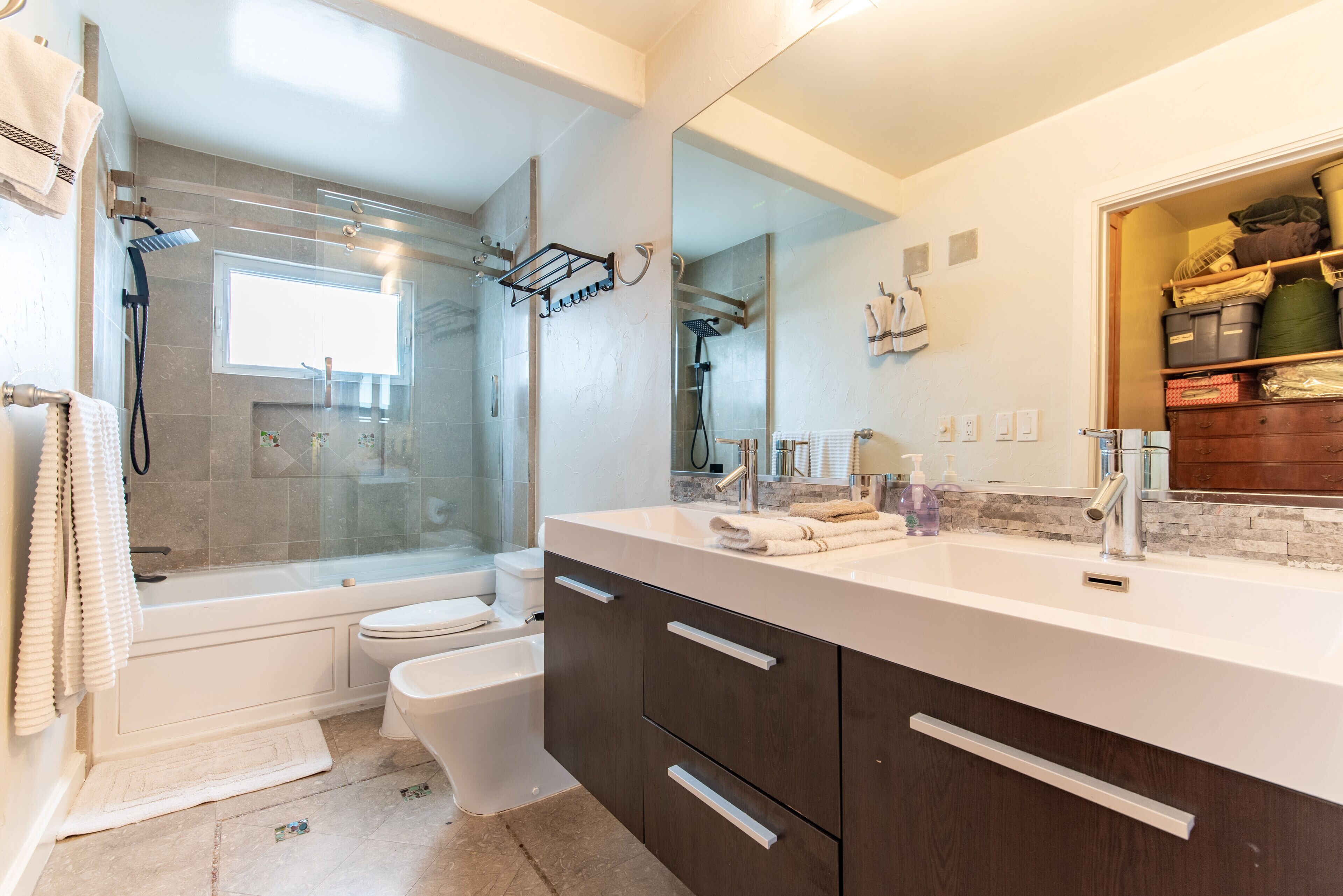 A modern bathroom with a glass-enclosed shower, a white toilet, a vanity with dark cabinets, and a large mirror.