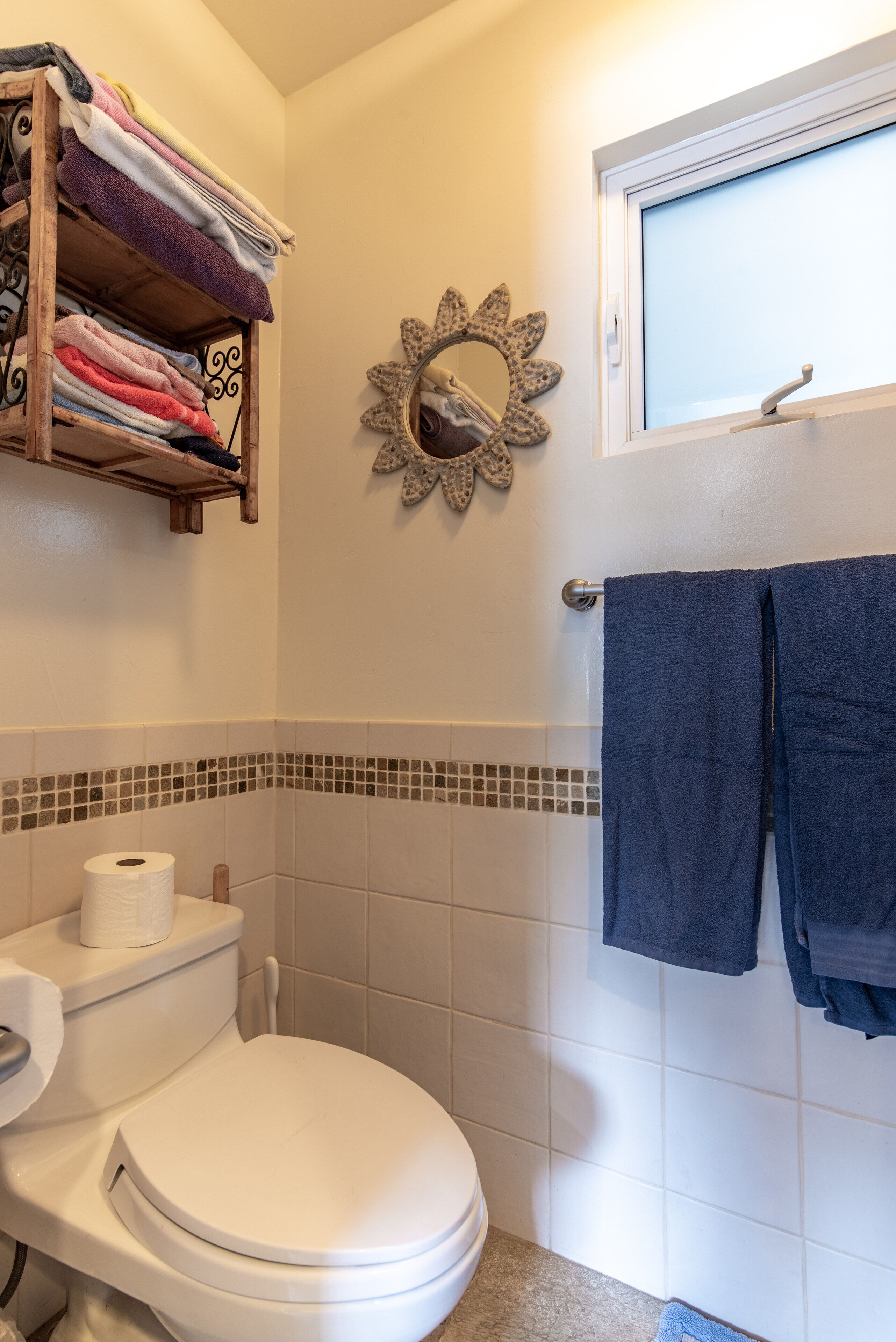 Un bagno con il water, un portascopino, uno specchio decorativo e una finestra.
