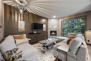 A modern living room with a sofa, coffee table, and fireplace. - Trail's Edge #7 | 3 Peaks Rentals (Sun Peaks)