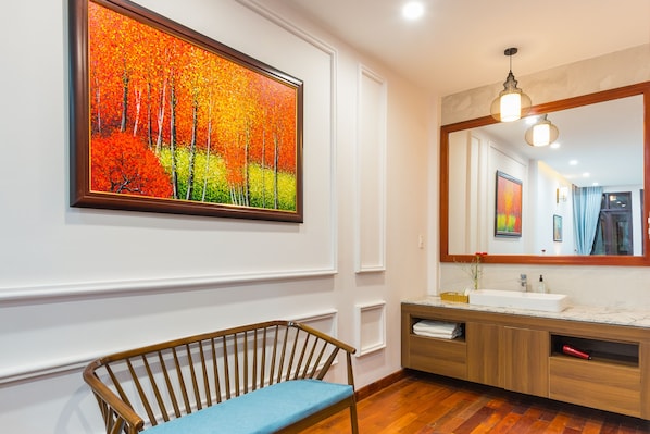 Un bagno moderno con una panca in legno, uno specchio grande e un quadro con alberi autunnali.