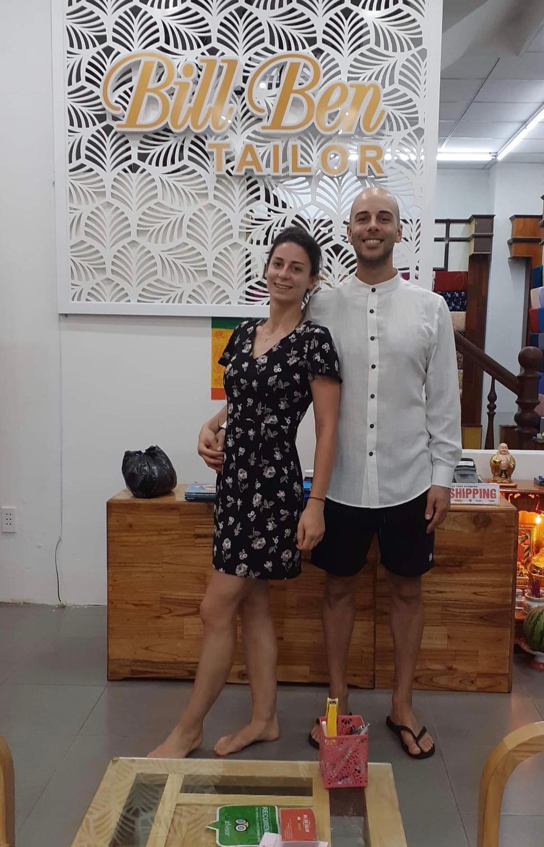 A man and a woman standing in a room with a decorative wall and a wooden counter.