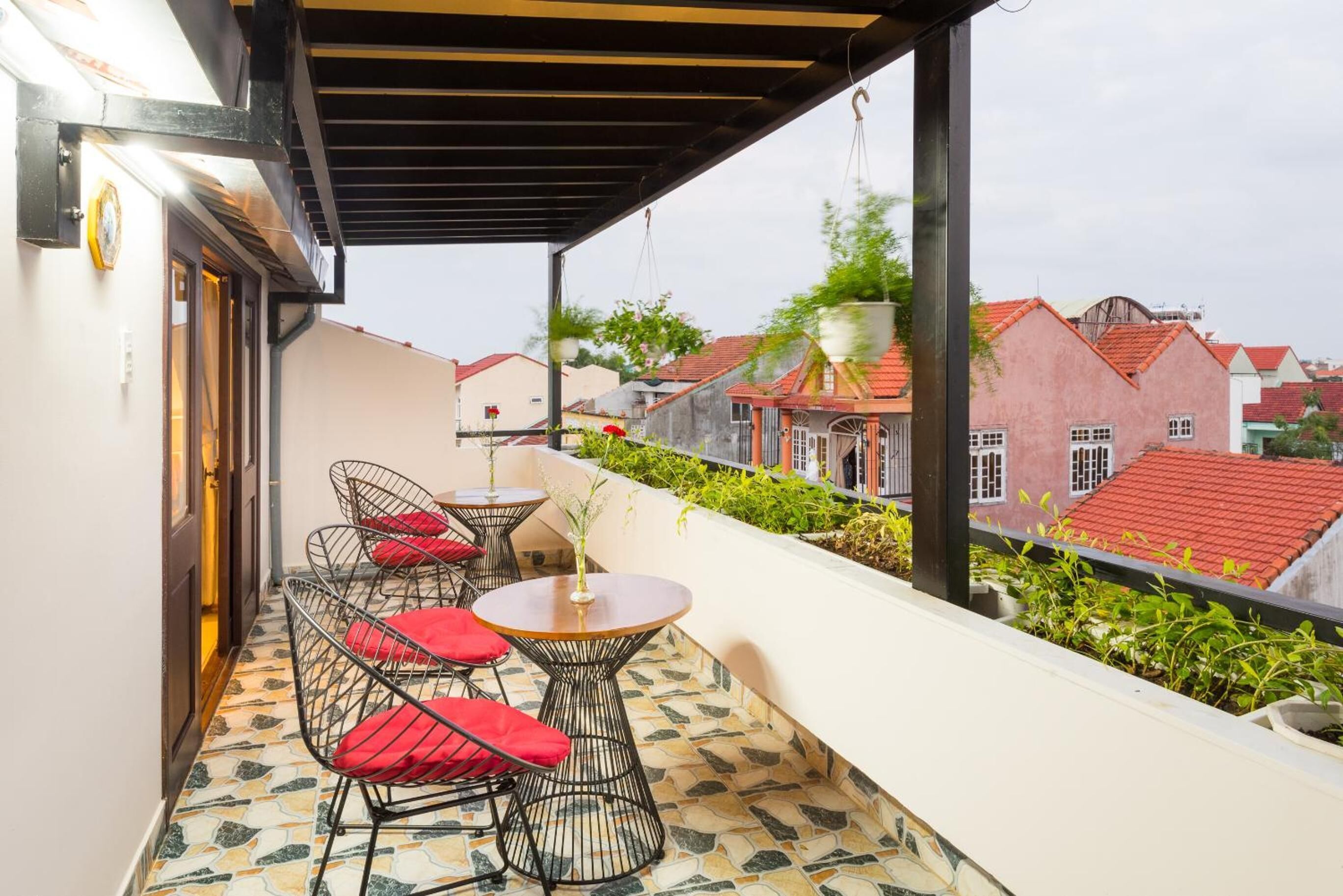 A balcony with a tiled floor, metal chairs with red cushions, and a small table.