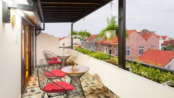 A balcony with a tiled floor, metal chairs with red cushions, and a small table.