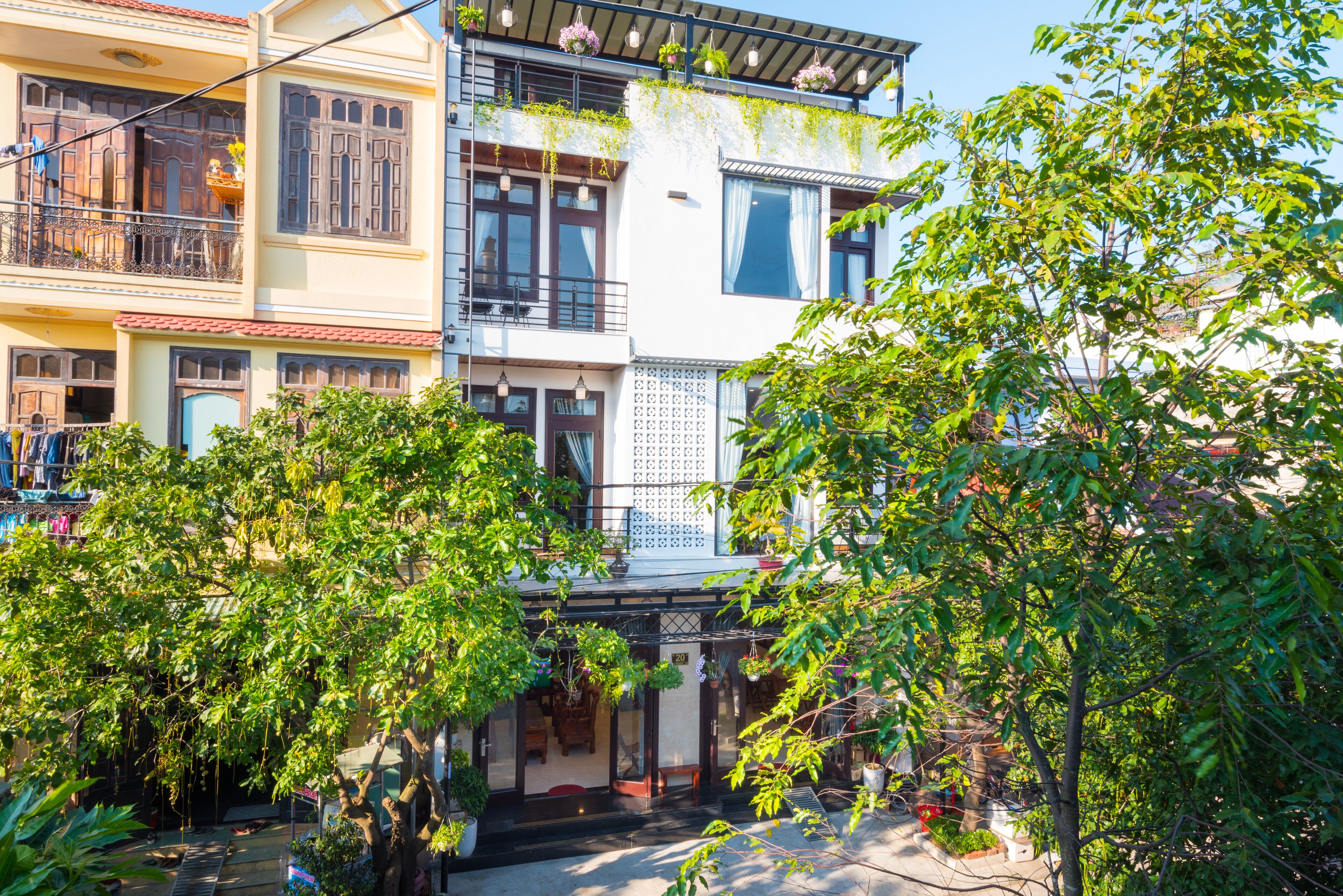 A multi-story building with balconies, a covered entrance, and lush greenery.
