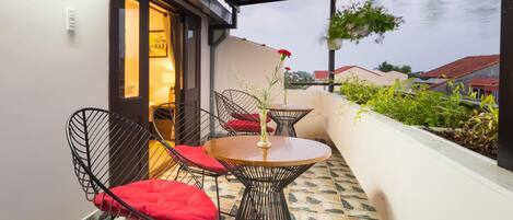 An outdoor patio with a round table and two chairs, a small vase with flowers, and a view of neighboring buildings.