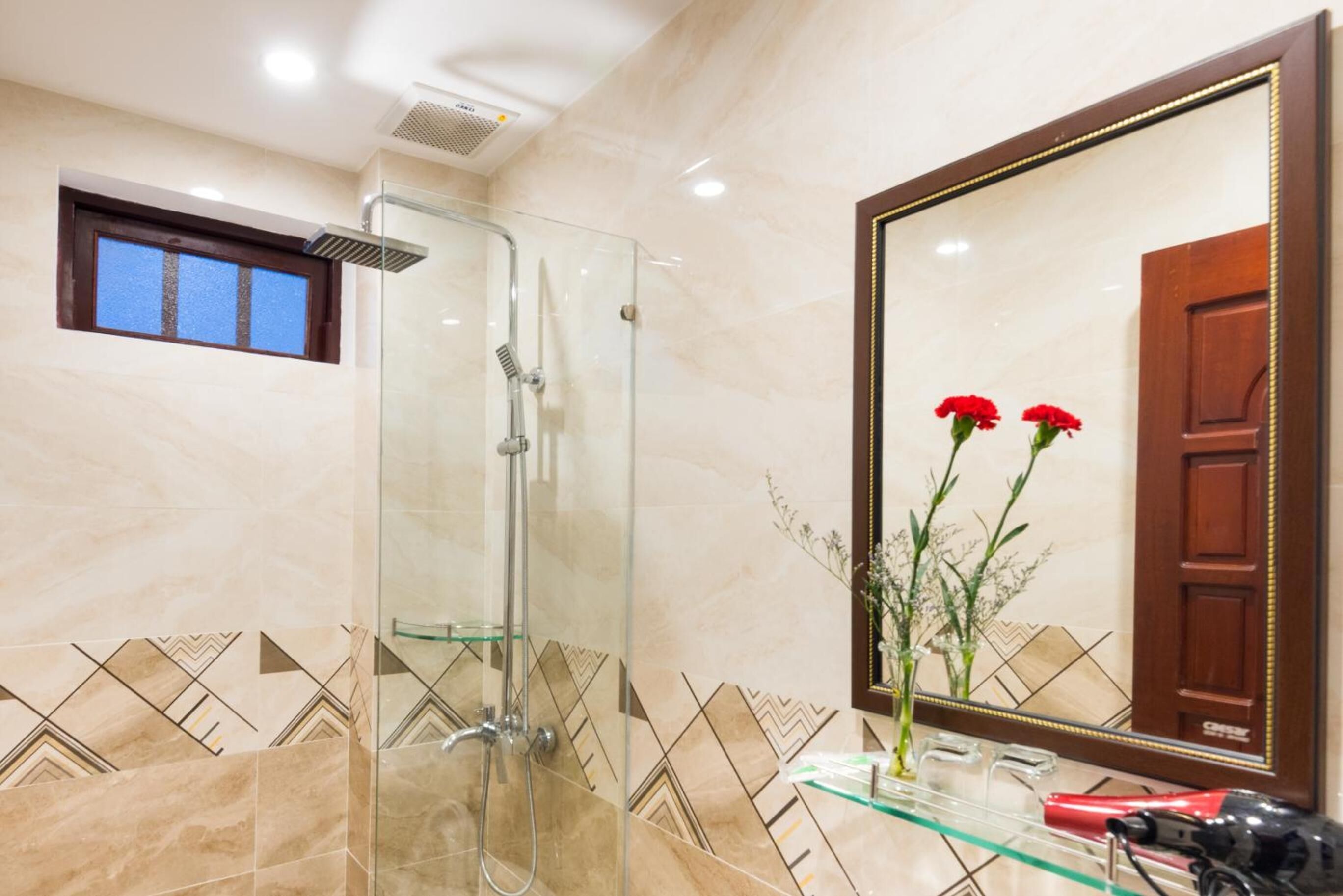 A bathroom with a glass-enclosed shower, a large mirror, and a vase with flowers.
