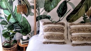 A bedroom with a large plant, a wooden headboard, and decorative pillows. - Treescape, Seascape Getaway (Ocean Grove)