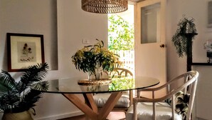 A dining area with a glass table, white chairs, and a hanging light fixture. - Treescape, Seascape Getaway (Ocean Grove)