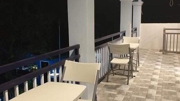 A covered outdoor seating area with tables and chairs, a tiled floor, and a railing.