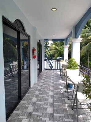 A covered balcony with a tiled floor, white chairs, and a fire extinguisher. - Azulea Lodging House Oslob (Oslob)
