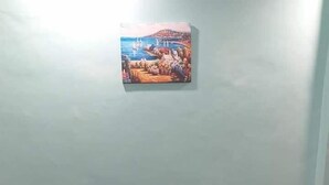 A brown sofa against a light blue wall with a painting of a coastal scene above it.