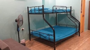 A bunk bed with a blue mattress, a standing fan, and a wooden floor.